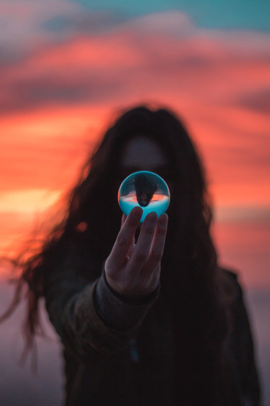 Woman with long hair in shadow at sunset holding glass sphere