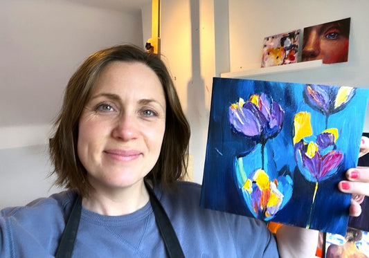 Louise Thompson holding a painting of blue and purple flowers